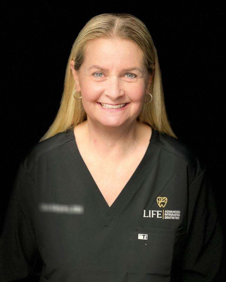 Smiling dentist in black scrubs, black background.